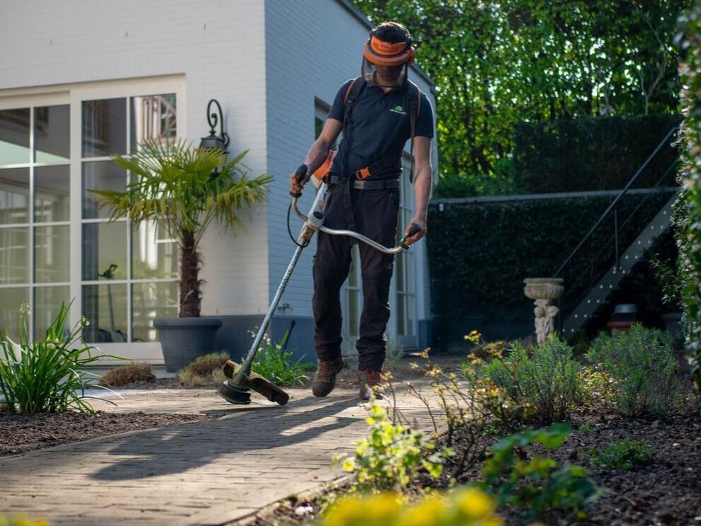 Man walking with a lawn trimmer along the edge of a path in a backyard